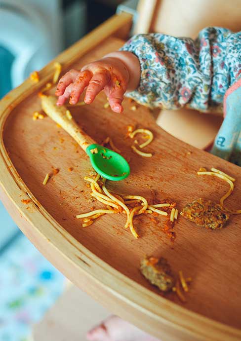 the hand of a child who is sitting on a high chair and reaching out for a spoon